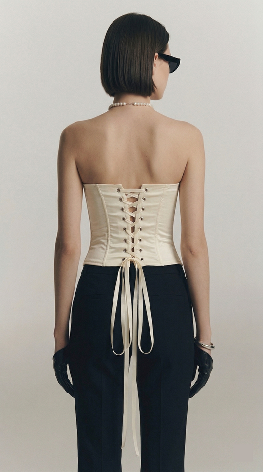 Woman wearing a strapless top with a corset-style back and black pants on a plain background